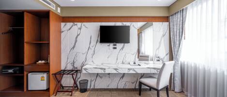 Habitación de hotel con cama, escritorio con televisor, armario, refrigerador pequeño y baño con espejo y cortinas.
