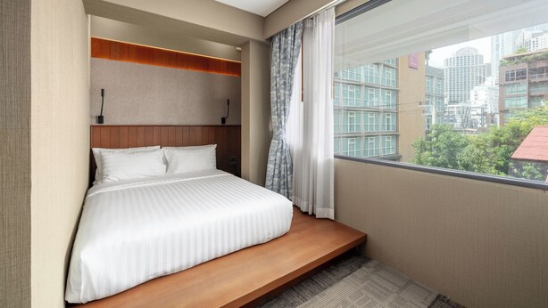 Habitació d'hotel moderna amb un llit gran, reposacapses integrat i vista a la ciutat a través d'una finestra gran.