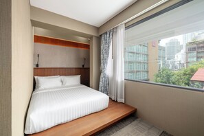 Een moderne hotelkamer met een groot bed, een vastgezet hoofdbord en uitzicht op de stad door een groot raam.