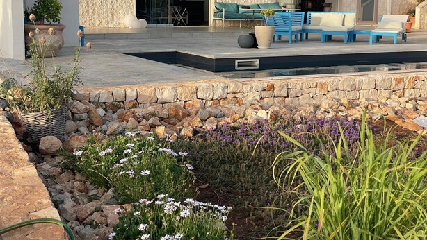 Zona exterior moderna amb piscina, parets de pedra i tendal blau.