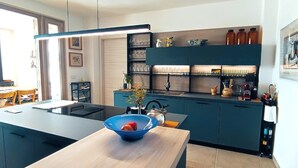 Cuina moderna amb una illa central, forn integrat i diferents utensilis de cuina a les estanteries.