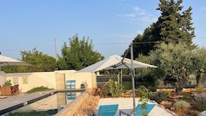 Zona de piscina amb un videt de pedra, gandules blaves i una pèrgola.