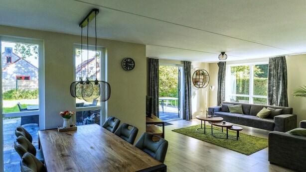 A spacious living area with a wooden dining table, sofas, and a large window offering a view of the outdoors. - Holiday home in Ewijk in a beautiful area (Ewijk)