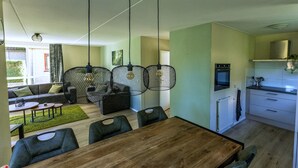 A modern living room with a dining table, sofa, and chairs. There is a kitchen area with a stove and cabinets. - Holiday home in Ewijk in a beautiful area (Ewijk)