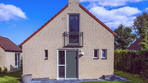 Une maison à deux étages, construite en briques, avec une porte verte, un petit balcon et un ciel d’un bleu limpide.