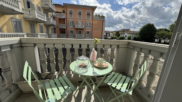 A balcony with a table and chairs, a vase with flowers, and a view of buildings in the background. - Charming Tuscan Home with Pool near Lucca (Lucca)