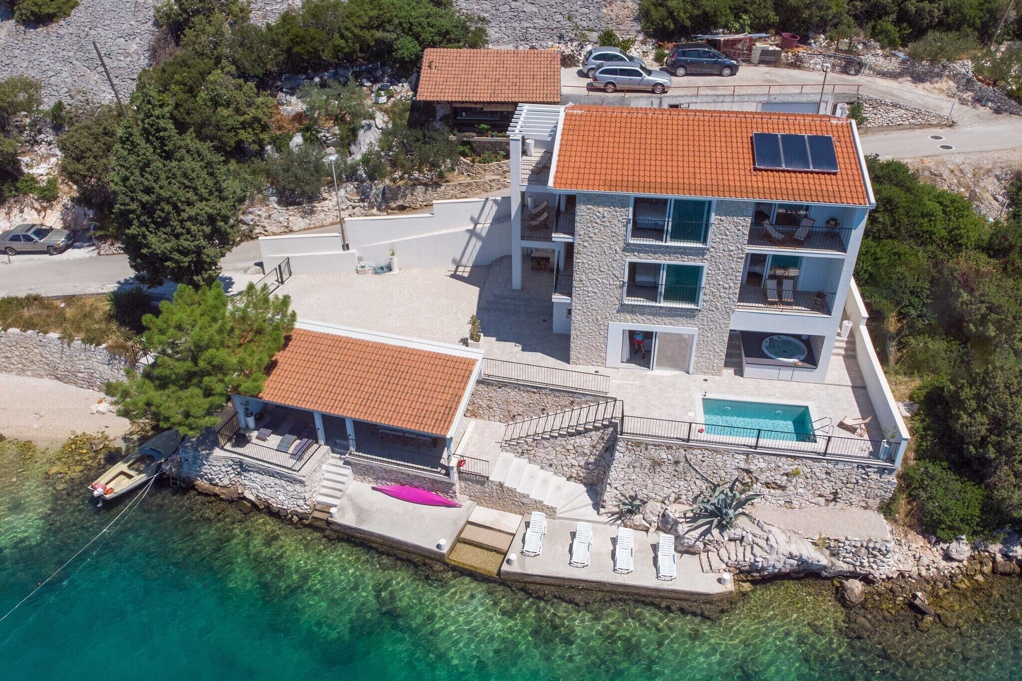 A multi-story coastal property with a swimming pool, a boat dock, and a stone facade.