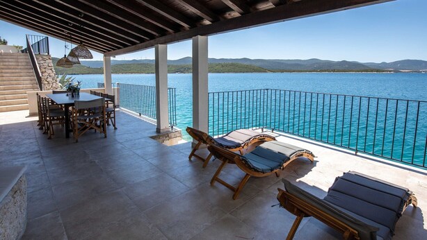 A covered outdoor area with a table and chairs, a poolside lounge, and a view of a lake and mountains. - Villa Simpleza - Six Bedroom Villa with Private Pool and Jacuzzi (Klek)