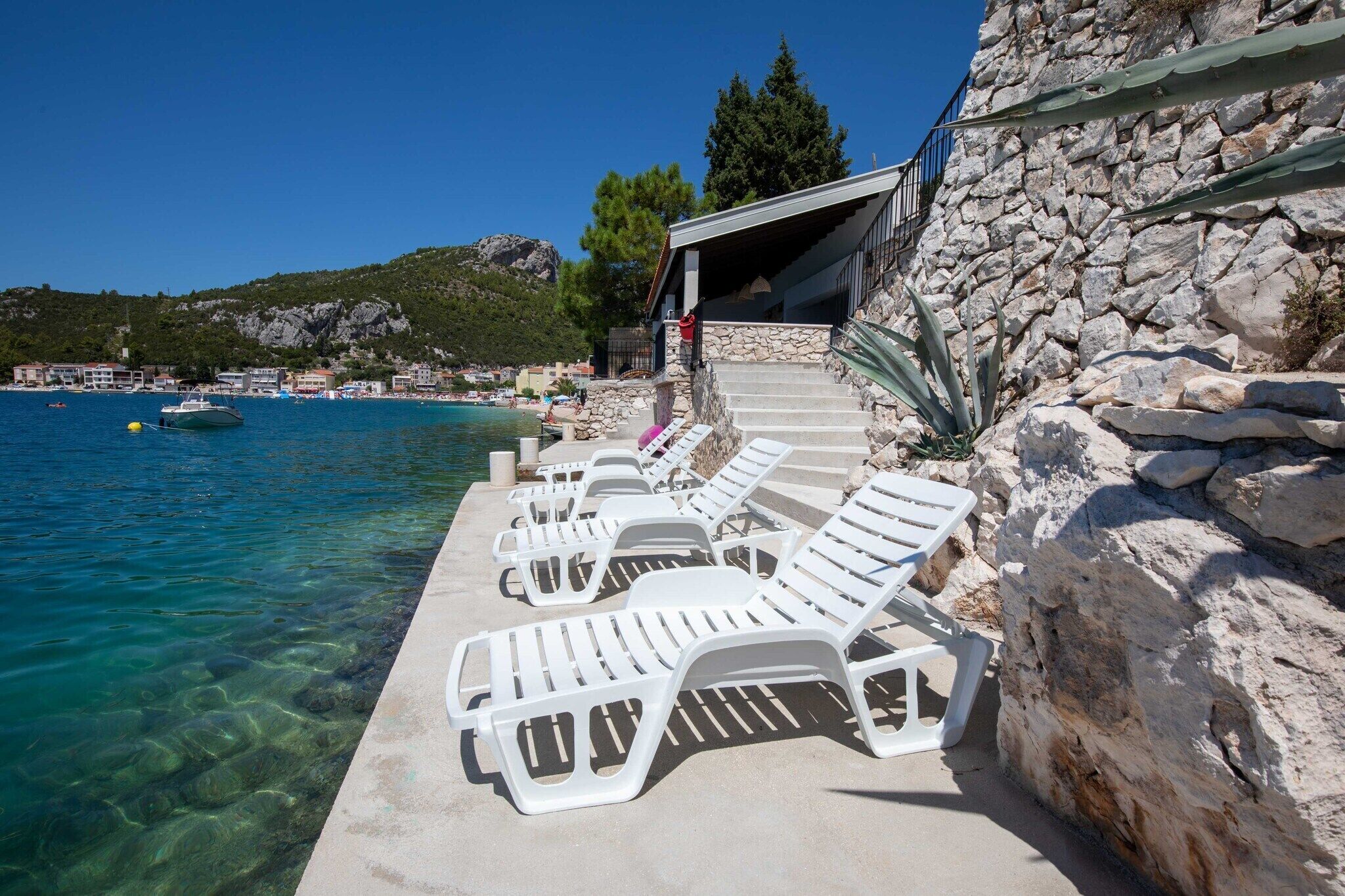 Un hôtel en bord de mer, doté d’une façade en pierre, d’une eau d’un bleu limpide et de chaises longues blanches au bord de la piscine.
