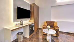 Ein modernes Zimmer mit einem an der Wand befestigten Flachbildfernseher, einer Holzkommode, einem kleinen Tisch mit Blumen in einer Vase und einem Papierkorb.