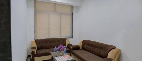 A living room with two brown sofas, a glass coffee table, and a window with blinds.