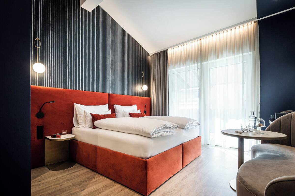 A modern hotel room with a large bed, a bedside table, a chair, and a window with curtains.
