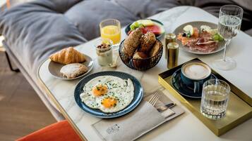 Una mesa con desayuno que incluye cruasanes, huevos, tostadas, fruta y bebidas.
