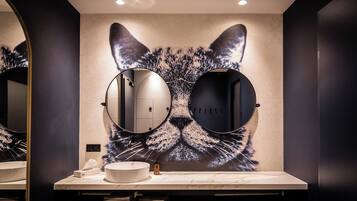 A bathroom with a large cat mural, two round mirrors, a white sink, and a towel rack.