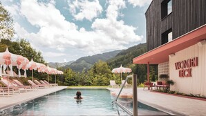 Une piscine entourée de chaises longues et de parasols, le tout bordé par un bâtiment sur lequel on peut voir une enseigne.