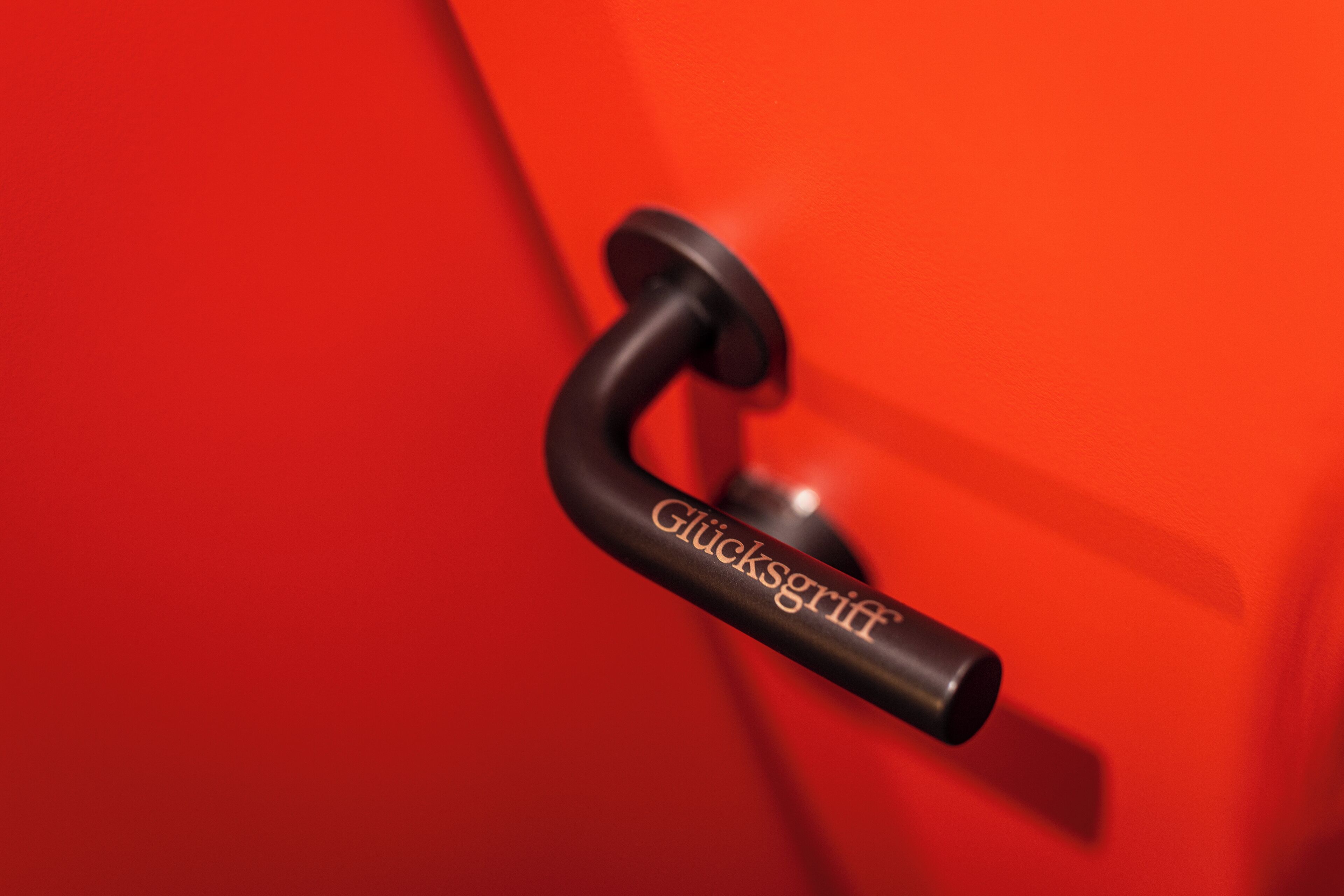 Primer plano de un pomo negro con el texto 'Glücksgriff' en una puerta roja.