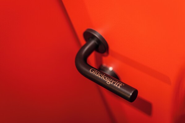 A close-up of a black door handle with the text "Glücksgriff" on a red door.