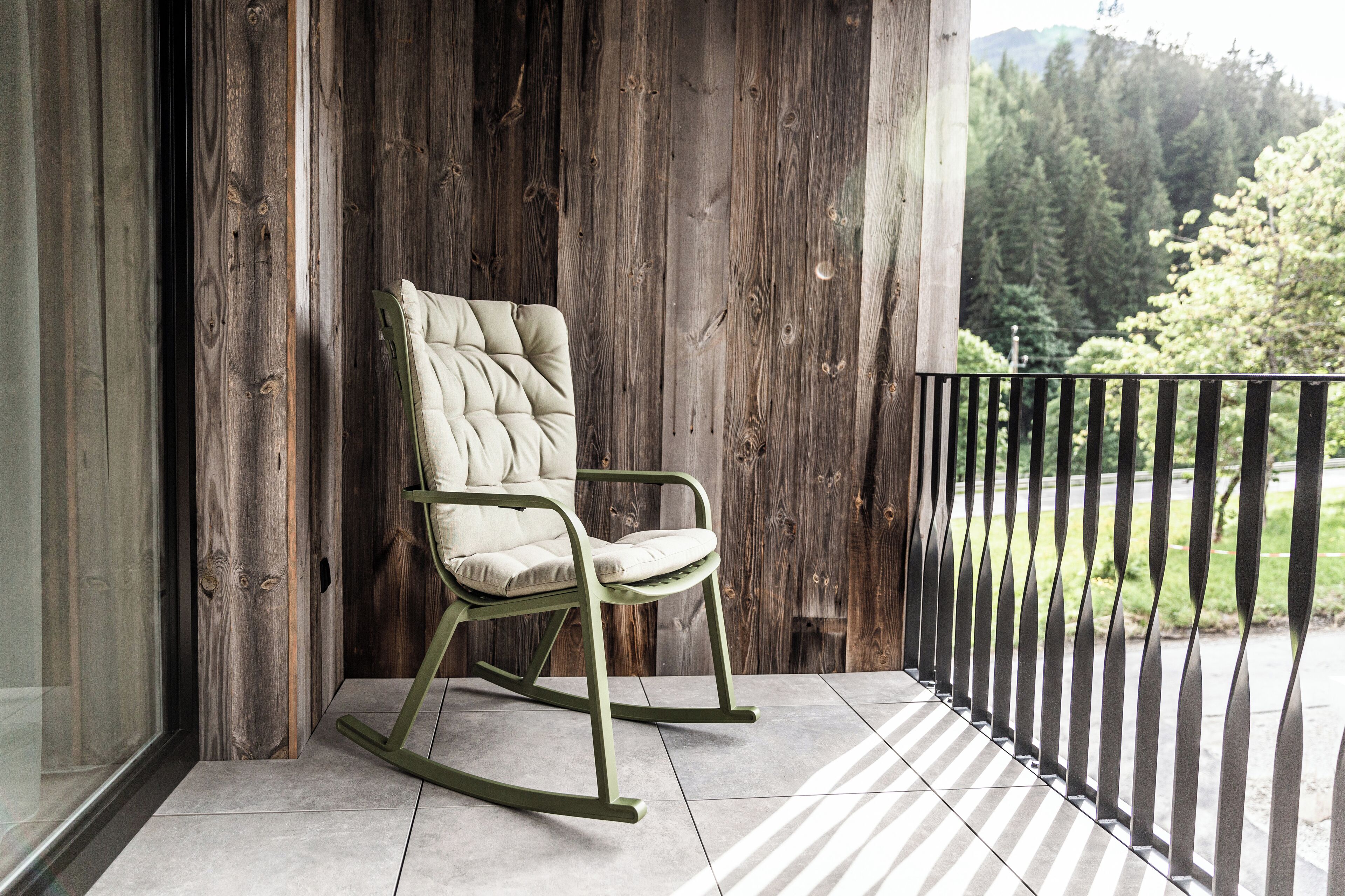 A rocking chair on a balcony with a wooden wall and a view of trees.