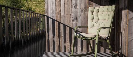 A rocking chair on a wooden deck with a metal railing, set against a wooden wall.