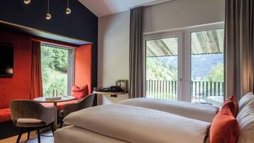 Habitación de hotel con cama, una mesita con silla, televisor y balcón con vistas al exterior.