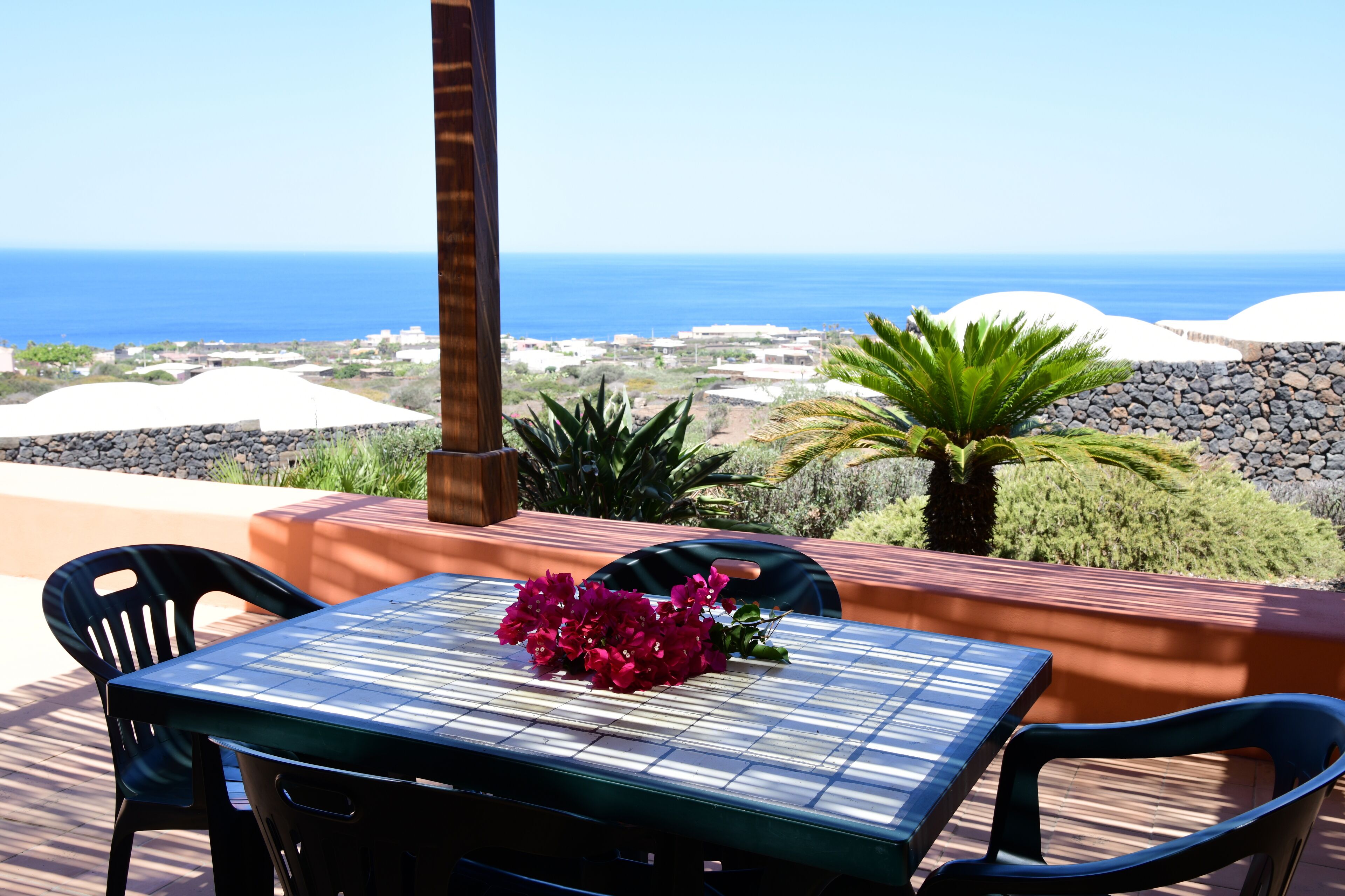 Una terraza con una mesa y sillas, una planta en maceta y vista al océano y edificios a lo lejos.