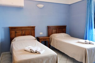 Habitación de hotel con dos camas, cabeceros de madera, una mesita de noche pequeña con cajón y aire acondicionado de pared.