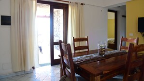 A dining area with a wooden table, four chairs, a glass with a flower arrangement, and a door leading outside. - Dammusi Sotto le Stelle (Pantelleria)