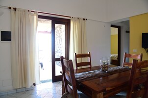 Un comedor con una mesa de madera, cuatro sillas, un vaso con un arreglo floral y una puerta que da al exterior.