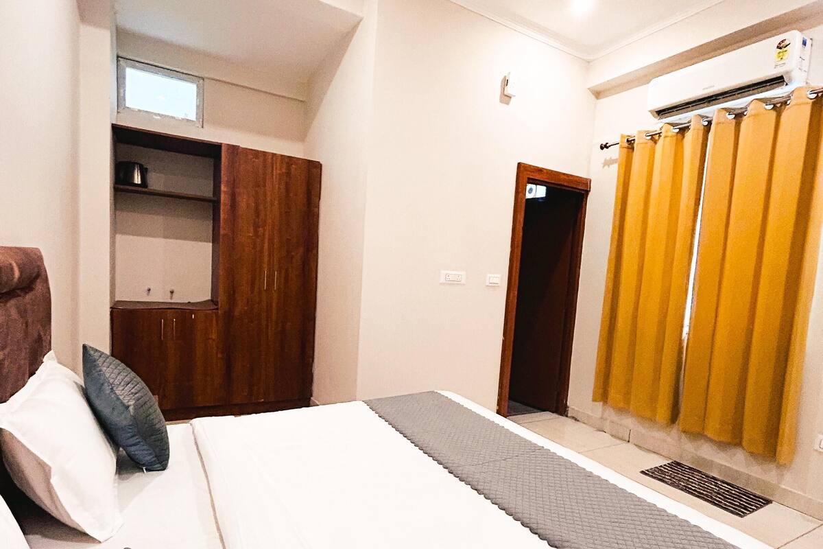 Une chambre à coucher avec un grand lit, une armoire, une salle de bain avec des rideaux jaunes et un ventilateur de plafond.