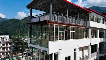 A multi-story building with large windows and balconies, set against a mountainous backdrop.