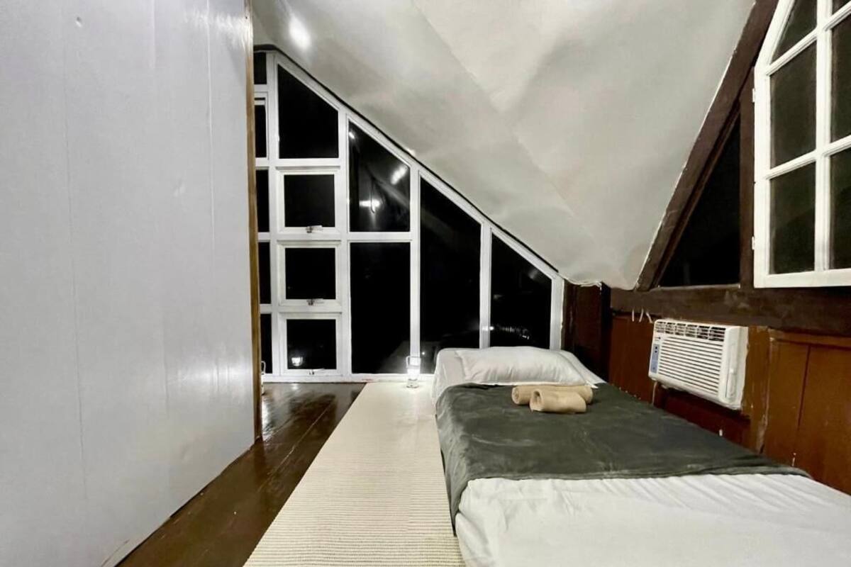 A bedroom with a sloped ceiling, a large window, a bed, and a radiator.