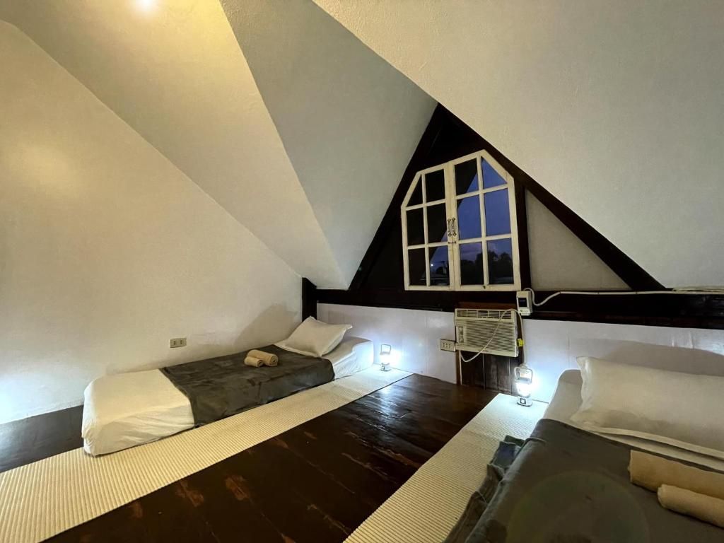 A small, triangular attic bedroom with two beds, a window, and a heater.