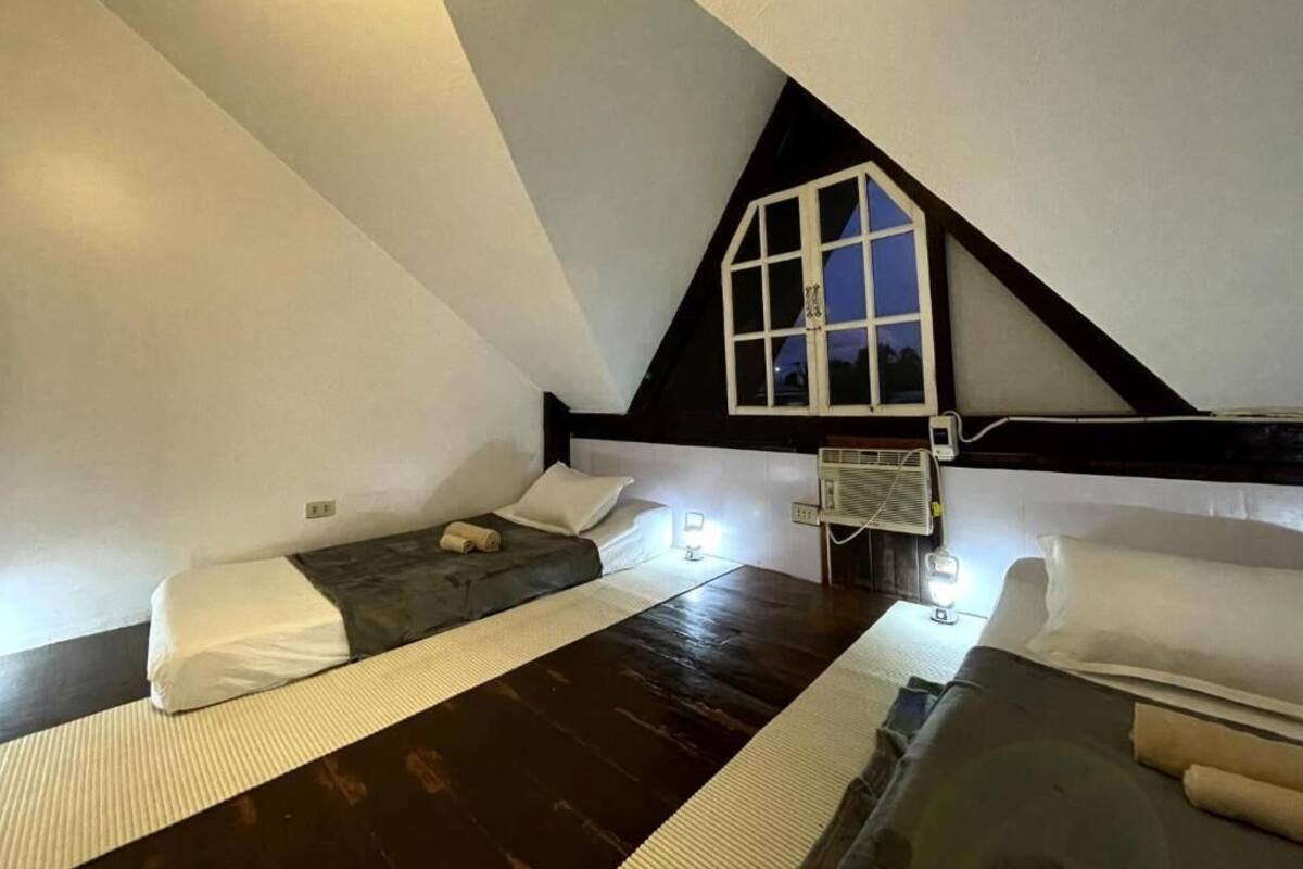 A small, triangular attic bedroom with two beds, a window, and a heater.