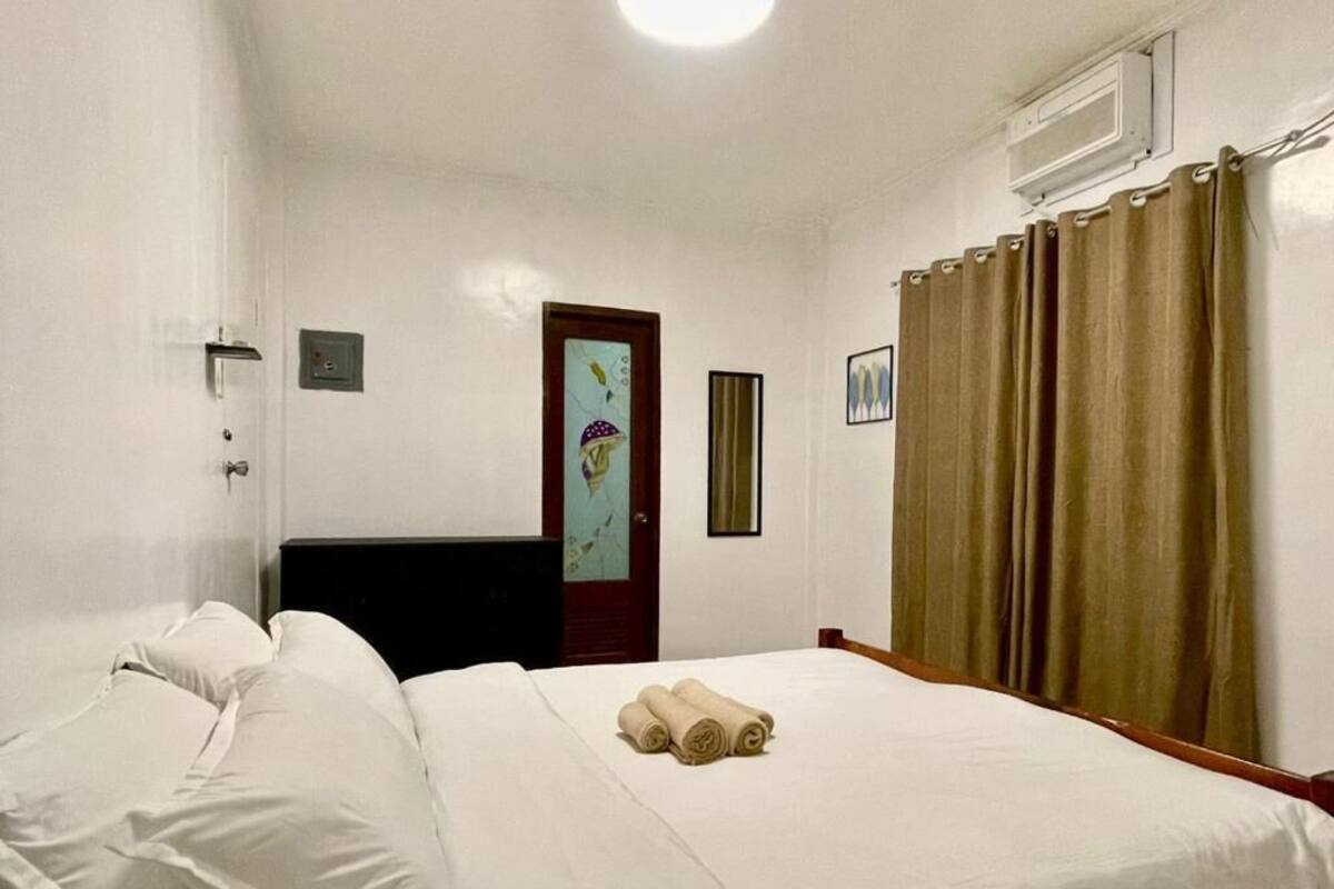 A hotel room with a bed, pillows, a door with a glass panel, a window, and curtains.
