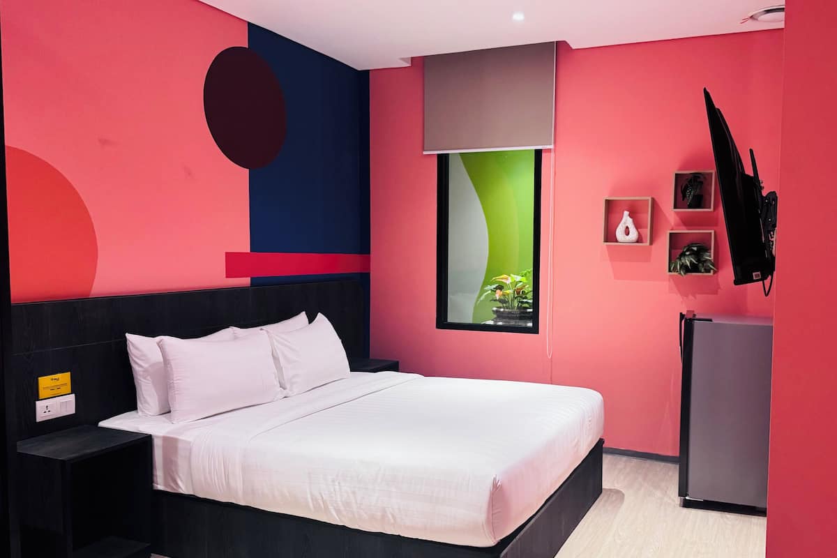 Un dormitorio moderno con una cama, una mesita de noche, un televisor montado en la pared y un refrigerador pequeño.