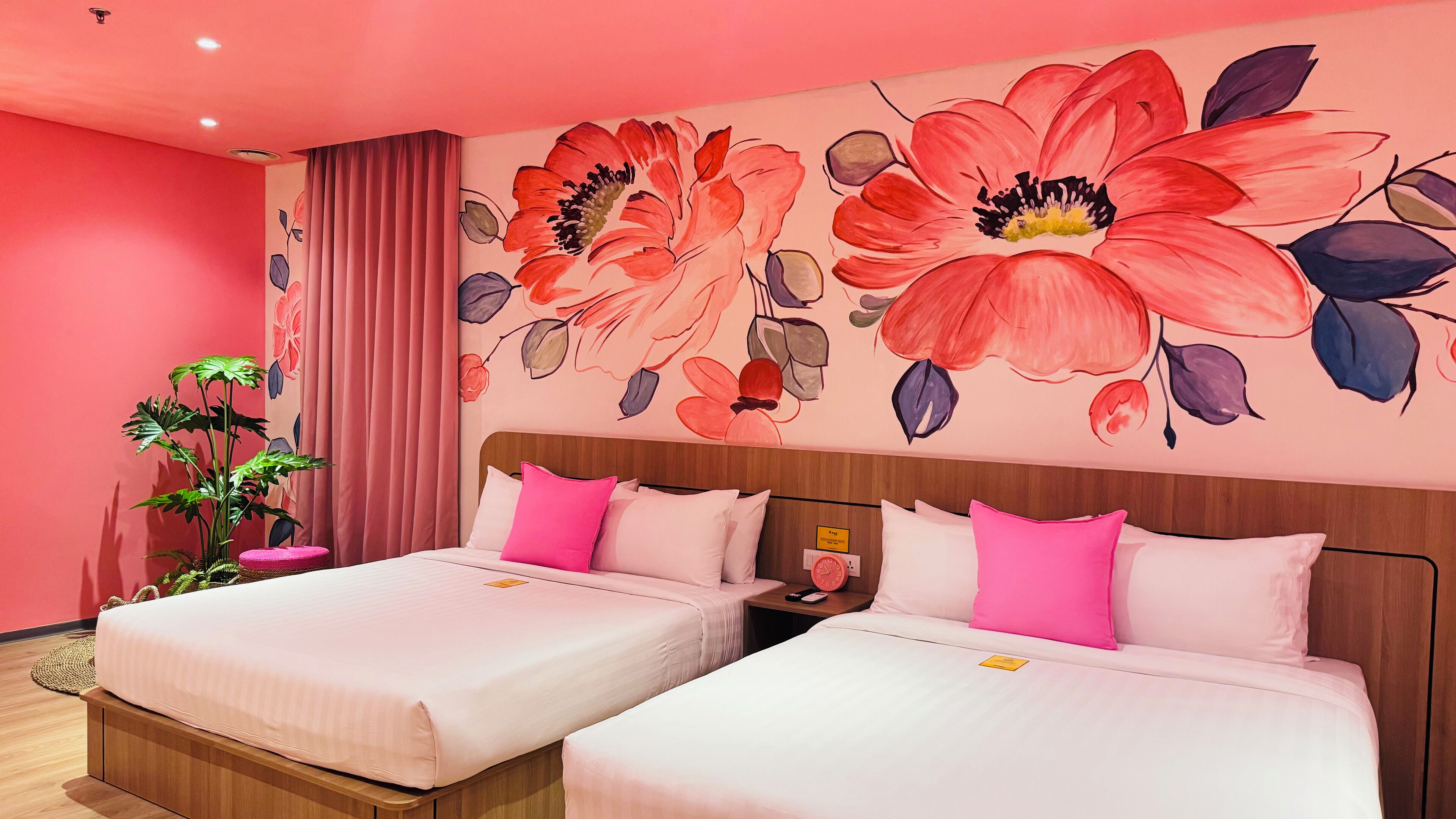 A hotel room with two beds, a large floral mural on the wall, a potted plant, and a wooden headboard.