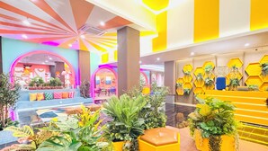 A brightly lit lobby with a central seating area, a reception desk with a plant display, and a colorful ceiling design. - Yellow Bee Resort Cililitan  (Jakarta)
