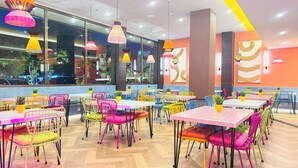 A brightly lit restaurant with colorful chairs and tables, large windows, and hanging lamps. - Yellow Bee Resort Cililitan  (Jakarta)