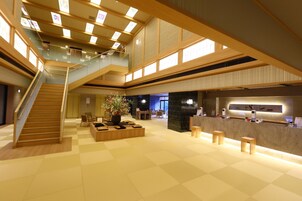 A spacious lobby with a wooden staircase, seating area, and a reception desk.