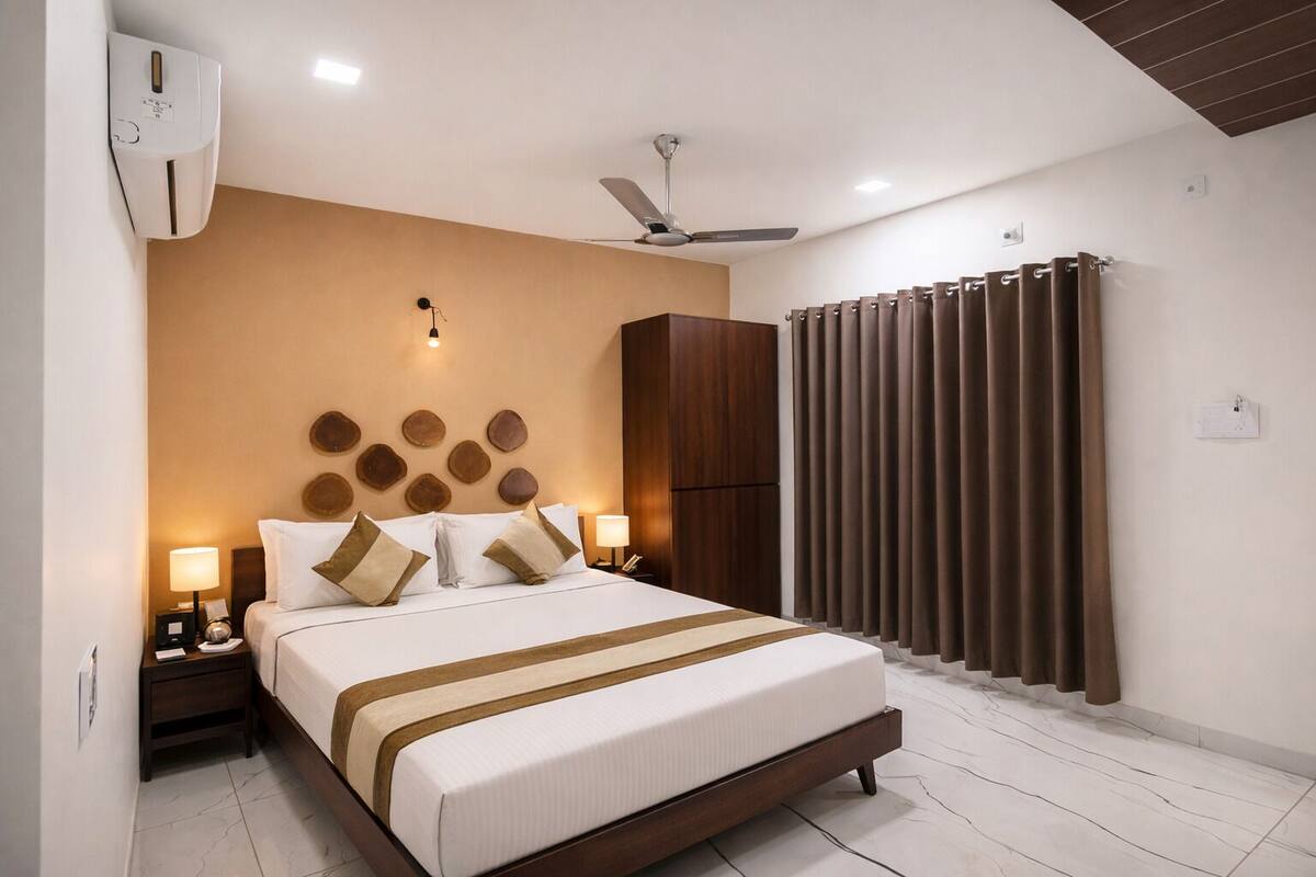 Ein Hotelzimmer mit Bett, Nachttischlampen, Deckenventilator, Wandairconditioner und einem Fenster mit Vorhängen.
