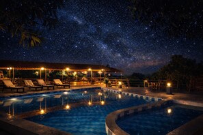 Ein Poolbereich bei Nacht mit Liegestühlen und einem beleuchteten Gebäude.