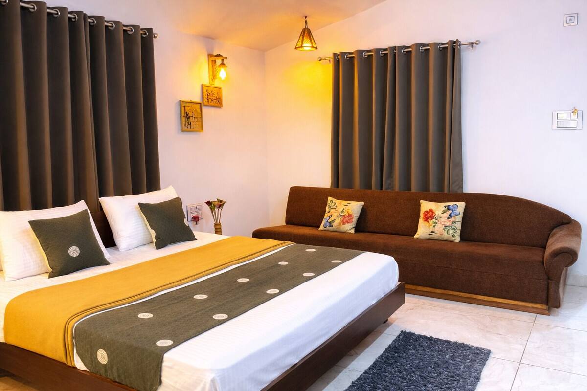 Ein Schlafzimmer mit einem Bett, einer Couch, Vorhängen, Wandleuchten und einem kleinen Tisch mit einer Vase.