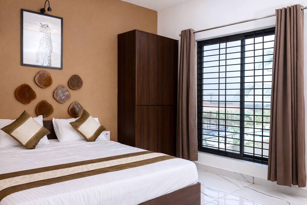 Ein Hotelzimmer mit einem großen Bett, einem Kleiderschrank, einem Fenster mit Vorhängen sowie einer Wand mit einem gerahmten Bild und Holzdekor.