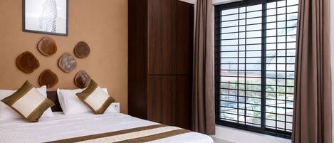 A hotel room with a large bed, a wardrobe, a window with curtains, and a wall with a framed picture and wooden decor.