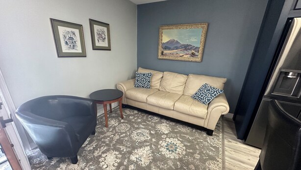 Ein Wohnzimmer mit einem beigen Sofa, zwei gemusterten Kissen, einem schwarzen Sessel, einem kleinen runden Tisch und einem großen Gemälde an der Wand.