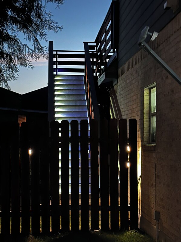 Una cerca de madera con listones verticales y una escalera de metal que lleva a un edificio.