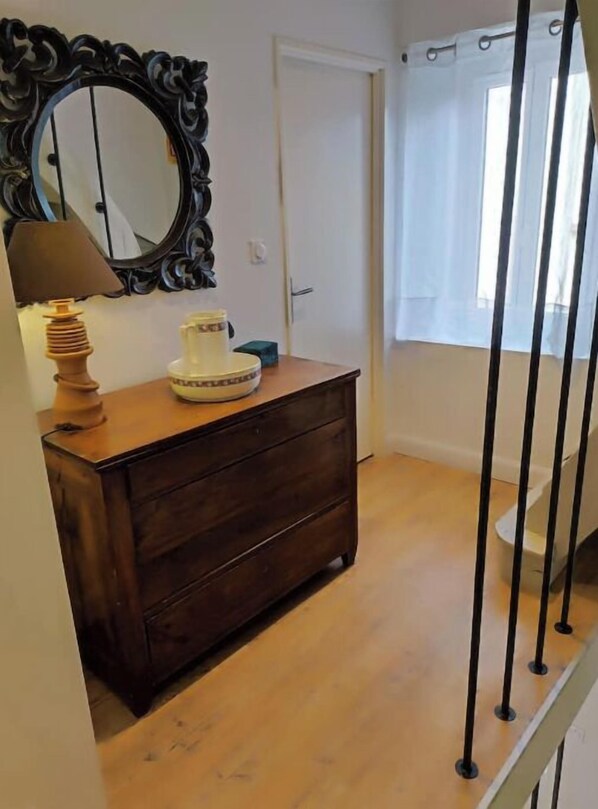 Une pièce comprenant une commode en bois, un miroir avec un cadre orné, une lampe et une fenêtre avec un rideau.