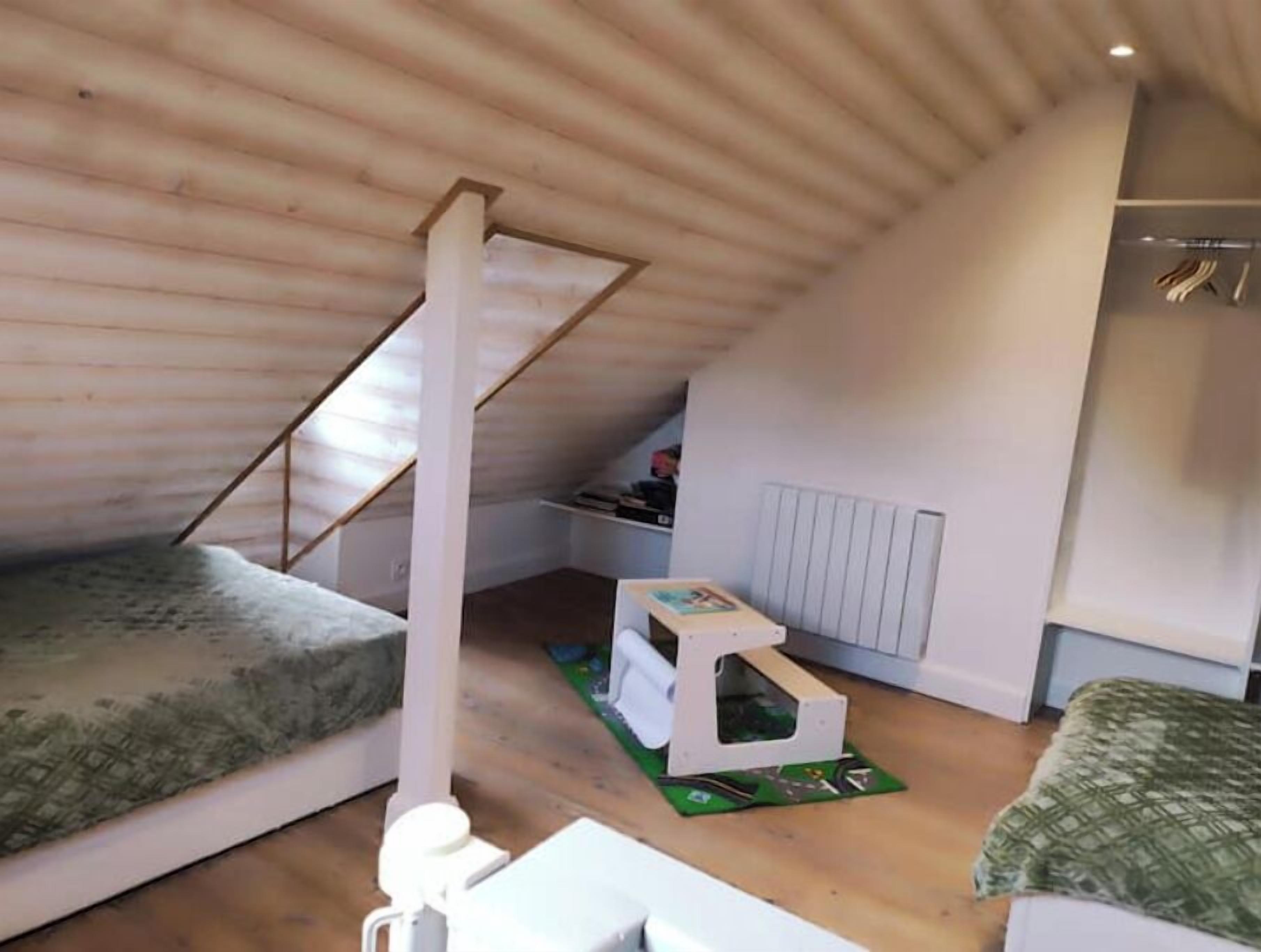 Un dormitorio bajo los tejados, con techo inclinado, una cama individual, una mesita y una casita para gatos.