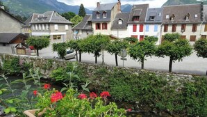 A quaint village with traditional European architecture, a stone wall, and a small stream.