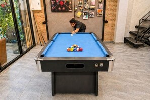 A pool table with balls, a person playing, and a brick wall with photos. - Friends Station Hostel & Cafe (Pattaya)